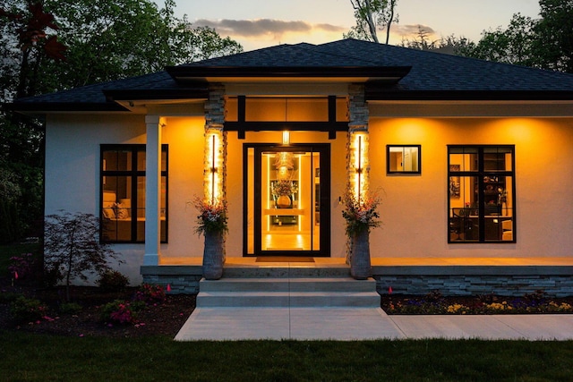 8159 Riverside Dr, Powell, OH 43065 - exterior entry at dusk with stucco siding, a porch, and roof with shingles