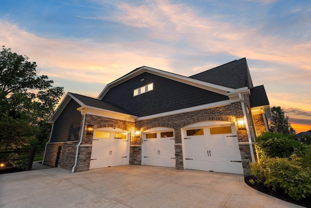 3624 Sparrow Ct, Hilliard, OH 43026 - property exterior at dusk with a garage, concrete driveway, stone siding, and brick siding