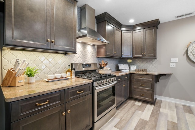 107 Willows End, Bellefontaine, OH 43311 - kitchen featuring stainless steel range with gas stovetop, wall chimney range hood, light wood-type flooring, dark brown cabinets, and light stone counters