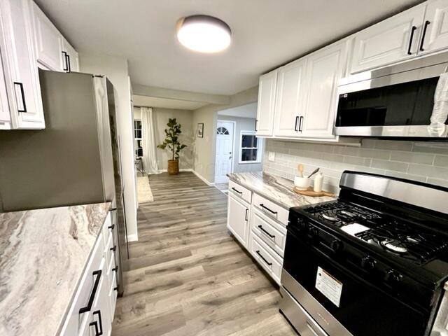79 N Main St, Jeffersonville, OH 43128 - kitchen featuring appliances with stainless steel finishes, baseboards, light wood-style floors, decorative backsplash, and white cabinets