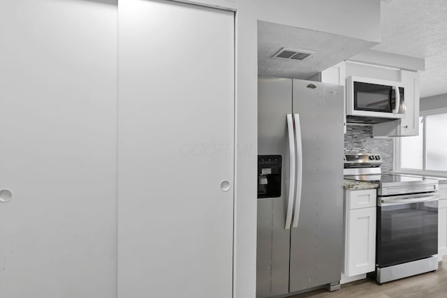 2505 Burgandy Ln Unit C, Columbus, OH 43232 - kitchen with appliances with stainless steel finishes, white cabinets, a textured ceiling, light wood-type flooring, and backsplash