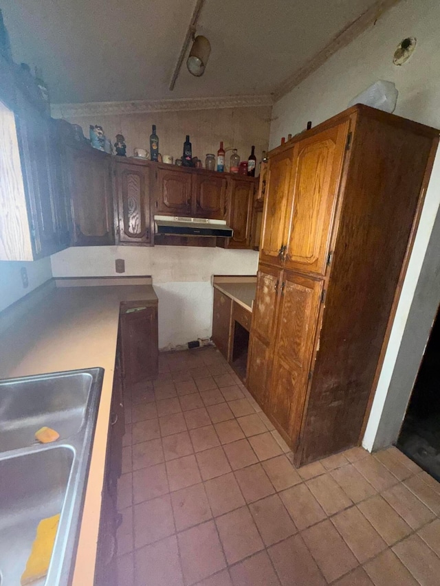 527 N 15th St, Coshocton, OH 43812 - kitchen with under cabinet range hood, light tile patterned floors, a sink, brown cabinets, and ornamental molding