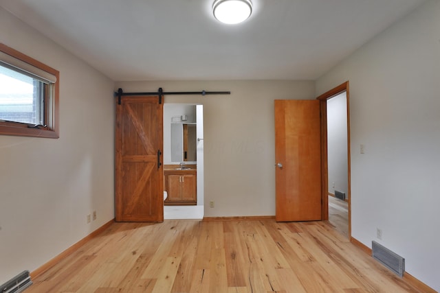 465 W Schrock Rd, Westerville, OH 43081 - unfurnished bedroom featuring a barn door, light wood-style flooring, a sink, baseboards, and connected bathroom