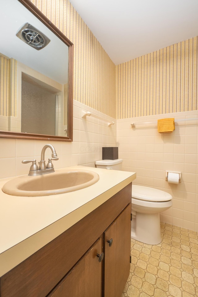 213 Kokosing Dr, Gambier, OH 43022 - bathroom featuring wallpapered walls, vanity, toilet, tile walls, and wainscoting