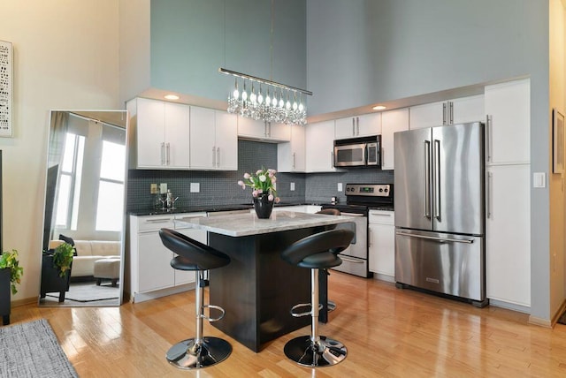 110 N 3rd St Unit 709, Columbus, OH 43215 - kitchen with stainless steel appliances, a towering ceiling, white cabinetry, light wood finished floors, and backsplash