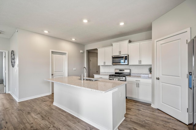 1002 Leslie Dr, Plain City, OH 43064 - kitchen featuring stainless steel appliances, a sink, a kitchen island with sink, wood finished floors, and white cabinetry
