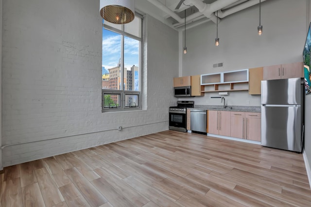 60 E Spring St Unit 327, Columbus, OH 43215 - kitchen with appliances with stainless steel finishes, a towering ceiling, light brown cabinets, brick wall, and open shelves