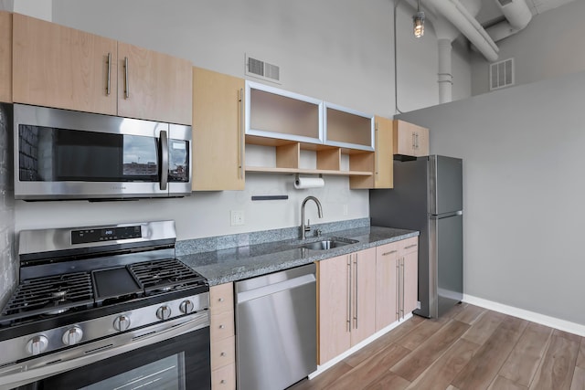 60 E Spring St Unit 327, Columbus, OH 43215 - kitchen featuring appliances with stainless steel finishes, light brown cabinetry, a sink, open shelves, and dark stone counters