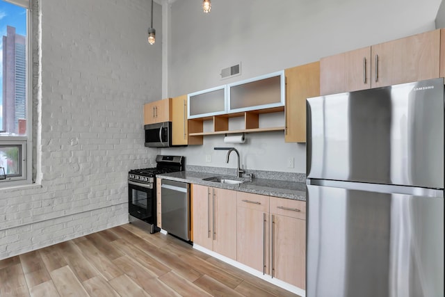60 E Spring St Unit 327, Columbus, OH 43215 - kitchen featuring appliances with stainless steel finishes, a sink, light brown cabinets, open shelves, and brick wall