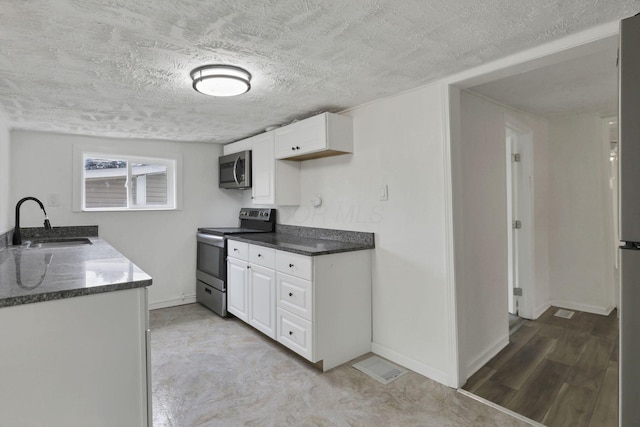 663 E Mound St, Circleville, OH 43113 - kitchen with appliances with stainless steel finishes, a sink, a textured ceiling, white cabinets, and baseboards