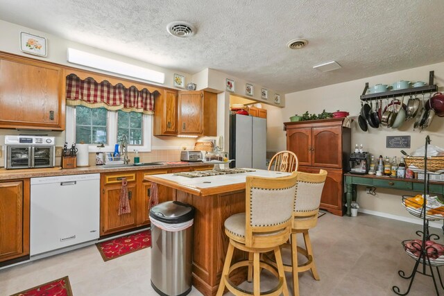 1235 Canteberry Ln, Mansfield, OH 44906 - kitchen featuring dishwasher, a sink, freestanding refrigerator, a breakfast bar area, and brown cabinets