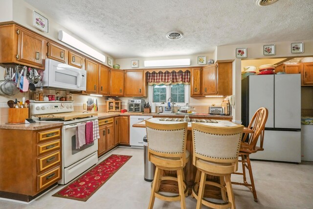 1235 Canteberry Ln, Mansfield, OH 44906 - kitchen featuring white appliances, a textured ceiling, brown cabinets, a kitchen breakfast bar, and a sink