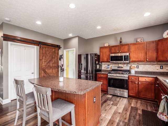 9148 Mccord Rd, Orient, OH 43146 - kitchen with stainless steel appliances, wood finished floors, a barn door, a kitchen bar, and decorative backsplash