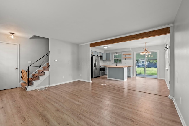1296 Bryson Rd, Columbus, OH 43224 - unfurnished living room featuring a chandelier, stairway, light wood-type flooring, and baseboards
