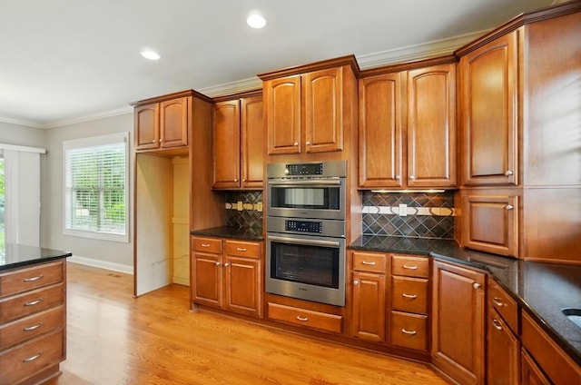4993 Denbigh Ct, Columbus, OH 43220 - kitchen featuring stainless steel double oven, light wood-style floors, dark stone countertops, crown molding, and brown cabinets