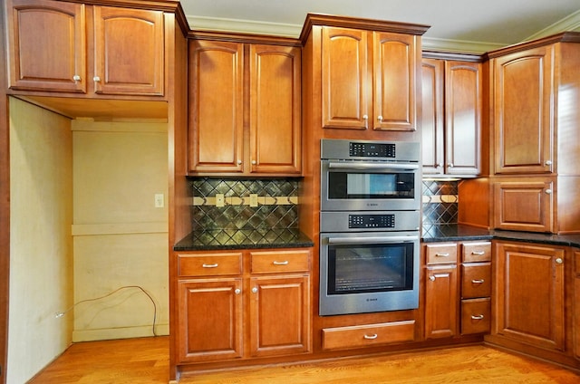 4993 Denbigh Ct, Columbus, OH 43220 - kitchen featuring stainless steel double oven, light wood-style floors, tasteful backsplash, brown cabinetry, and dark stone counters
