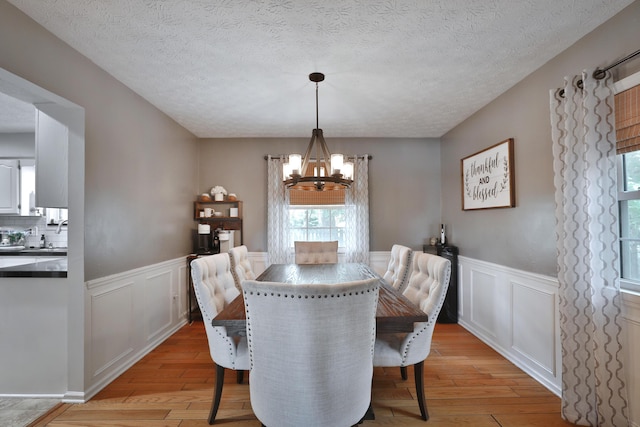 5255 Dory Ln, Columbus, OH 43235 - dining area with a chandelier, light wood-style flooring, wainscoting, a textured ceiling, and a decorative wall