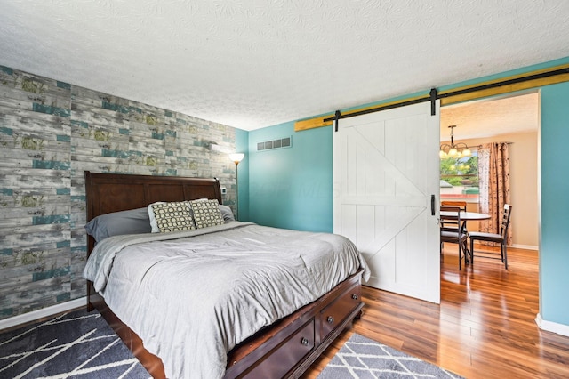 6588 Ethan Dr, Reynoldsburg, OH 43068 - bedroom featuring a barn door, an accent wall, baseboards, wood finished floors, and a textured ceiling