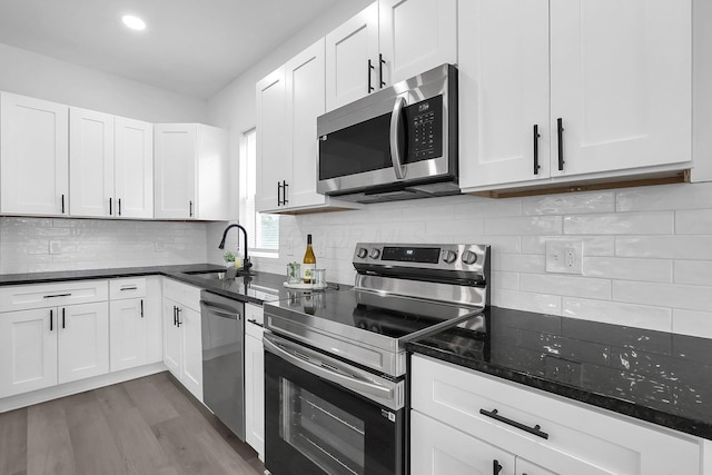 1191 Seymour Ave, Columbus, OH 43206 - kitchen with appliances with stainless steel finishes, a sink, white cabinetry, wood finished floors, and dark stone counters