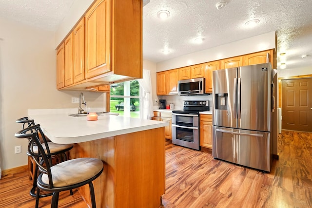 19160 Coshocton Rd, Mount Vernon, OH 43050 - kitchen featuring stainless steel appliances, a textured ceiling, a sink, a peninsula, and light wood finished floors