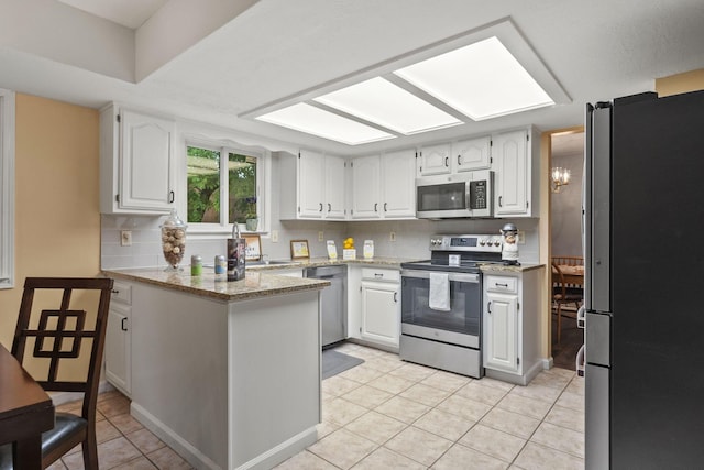 4129 Leitrim Ct, Dublin, OH 43016 - kitchen featuring appliances with stainless steel finishes, a peninsula, light tile patterned floors, white cabinetry, and backsplash