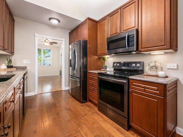 38 Ironclad Dr, Columbus, OH 43213 - kitchen with stainless steel appliances, wood finished floors, light stone countertops, brown cabinets, and baseboards