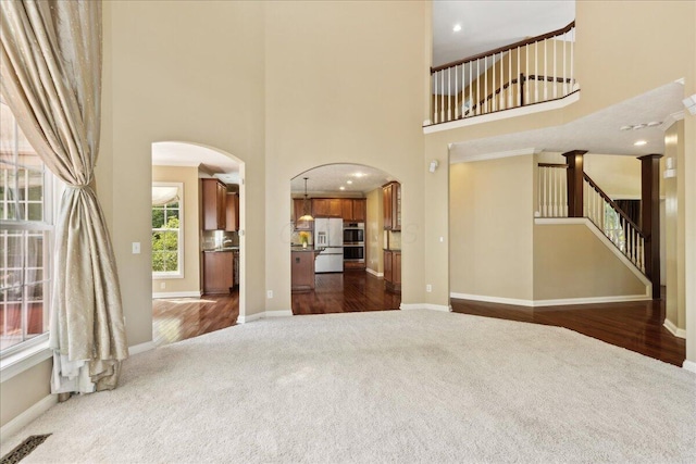 3144 Abbey Knoll Dr, Lewis Center, OH 43035 - unfurnished living room featuring dark colored carpet, arched walkways, a towering ceiling, baseboards, and dark wood-style floors