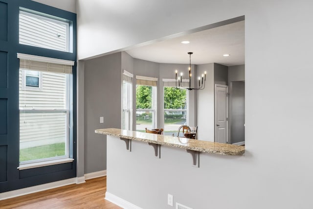6458 Tallman Ct, Canal Winchester, OH 43110 - kitchen featuring a chandelier, a breakfast bar, light stone counters, light wood-style flooring, and baseboards