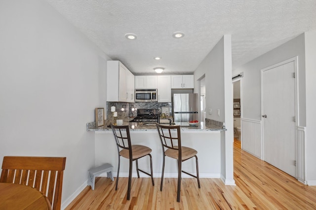 1994 Hoadley Dr Unit 7C, Columbus, OH 43228 - kitchen featuring appliances with stainless steel finishes, light wood-style floors, a breakfast bar area, white cabinets, and a textured ceiling