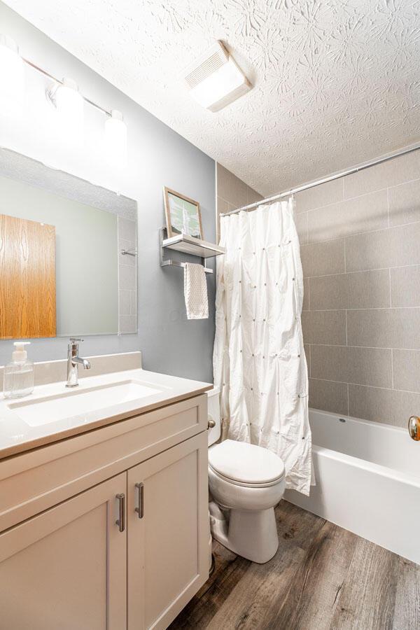 2643 Westrock Dr, Hilliard, OH 43026 - bathroom with wood finished floors, toilet, vanity, a textured ceiling, and shower / bathtub combination with curtain