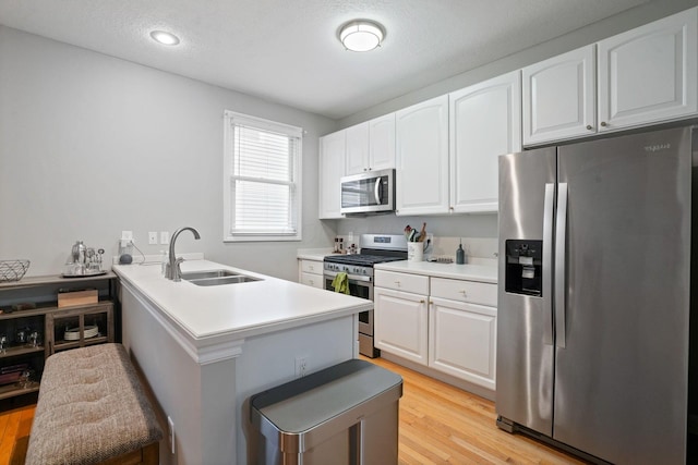 963 Delaware Ave, Columbus, OH 43201 - kitchen with stainless steel appliances, a sink, white cabinets, light wood finished floors, and a peninsula