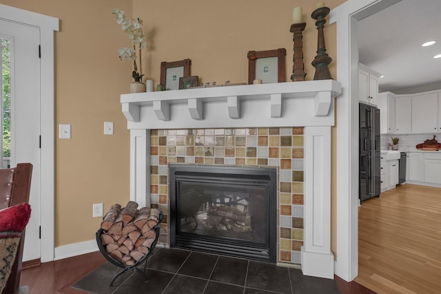 14980 Robins Rd, Johnstown, OH 43031 - detailed view of black refrigerator with ice dispenser, a fireplace, decorative backsplash, wood finished floors, and dishwashing machine