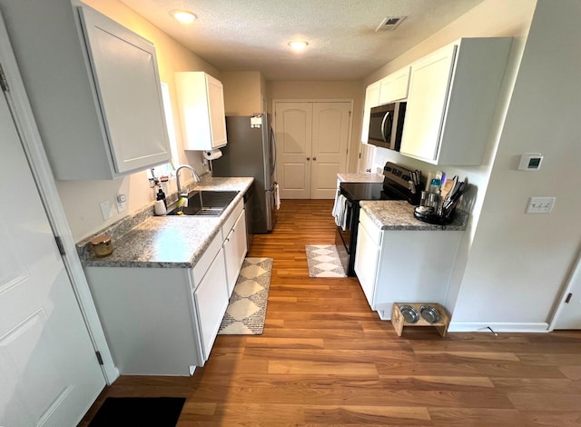 324 Genoa Rd, Commercial Point, OH 43116 - kitchen with a sink, appliances with stainless steel finishes, light wood finished floors, white cabinets, and a textured ceiling
