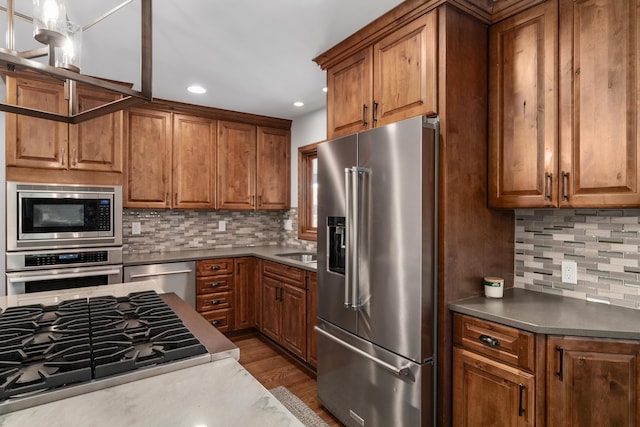 2656 Fair Ave, Columbus, OH 43209 - kitchen with appliances with stainless steel finishes, brown cabinetry, backsplash, wood finished floors, and recessed lighting