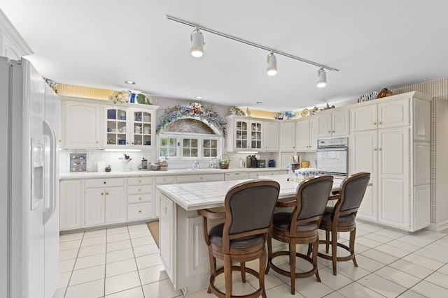 8039 Crossgate Ct S, Dublin, OH 43017 - kitchen featuring white fridge with ice dispenser, light tile patterned floors, a center island, glass insert cabinets, and a breakfast bar