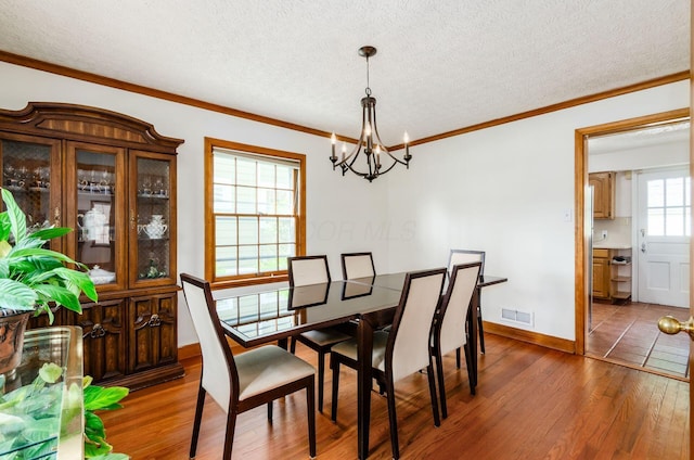 193 N Remington Rd, Columbus, OH 43209 - dining room with wood-type flooring, a chandelier, a textured ceiling, crown molding, and baseboards