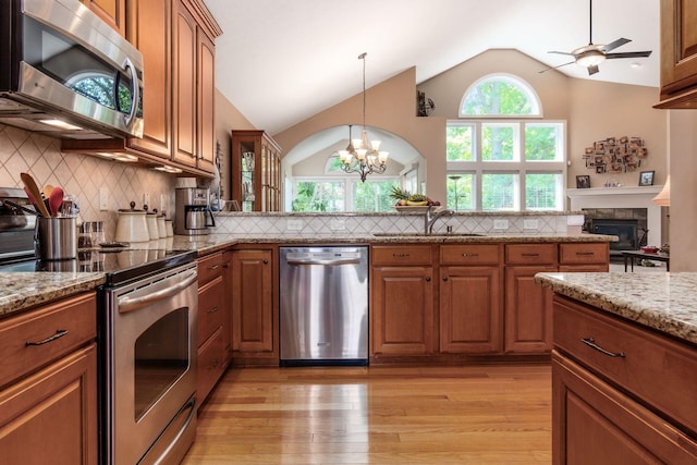 165 Tinley Park Cir, Delaware, OH 43015 - kitchen featuring appliances with stainless steel finishes, brown cabinetry, vaulted ceiling, a tile fireplace, and light wood-style floors