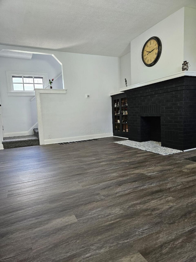 2889 E 12th Ave, Columbus, OH 43219 - unfurnished living room featuring dark wood-style flooring, baseboards, a textured ceiling, stairs, and a fireplace