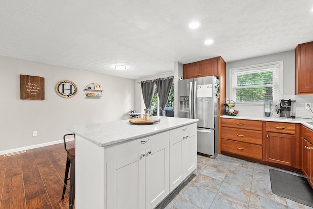 4373 Valley Quail Blvd S, Westerville, OH 43081 - kitchen with stainless steel refrigerator with ice dispenser, a textured ceiling, a kitchen bar, a kitchen island, and brown cabinets
