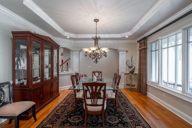 7699 Clear Creek Ct, Blacklick, OH 43004 - dining area with ornate columns, a chandelier, light wood-style floors, a tray ceiling, and crown molding