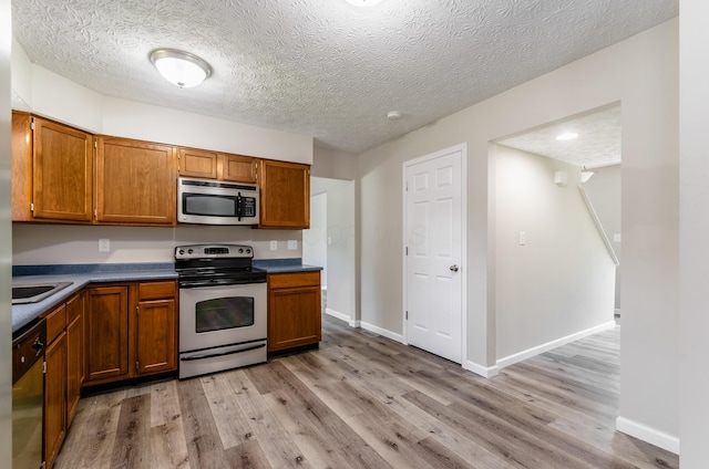 3248 Medoma Dr, Columbus, OH 43204 - kitchen with appliances with stainless steel finishes, light wood-style flooring, brown cabinetry, dark countertops, and a textured ceiling