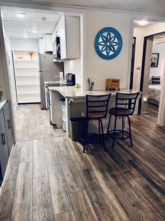 3037 La Vista Dr Unit 39, Columbus, OH 43204 - kitchen featuring hardwood / wood-style flooring, stainless steel appliances, a kitchen bar, a peninsula, and white cabinetry