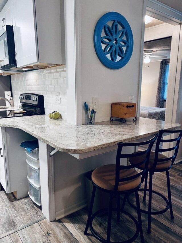 3037 La Vista Dr Unit 39, Columbus, OH 43204 - kitchen featuring appliances with stainless steel finishes, wood finished floors, backsplash, light stone countertops, and a breakfast bar area