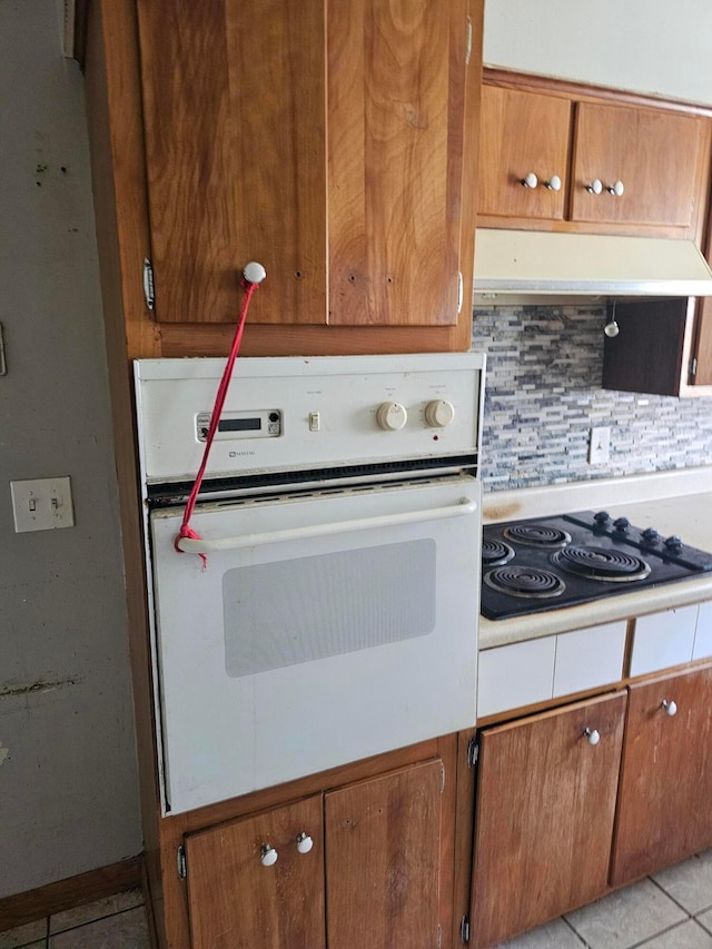 271 Carilla Ln, Columbus, OH 43228 - kitchen with oven, black electric cooktop, under cabinet range hood, backsplash, and light tile patterned floors