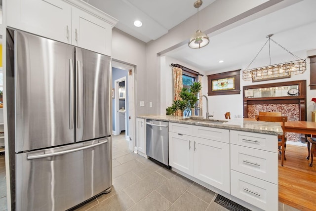 663 Wilson Ave, Columbus, OH 43205 - kitchen with appliances with stainless steel finishes, a sink, white cabinets, light stone counters, and hanging light fixtures