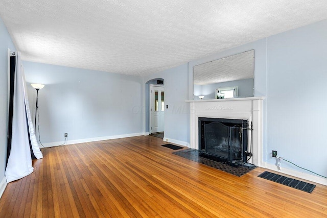 644 Eastmoor Blvd, Columbus, OH 43209 - unfurnished living room with a textured ceiling, a fireplace with flush hearth, arched walkways, hardwood / wood-style flooring, and baseboards