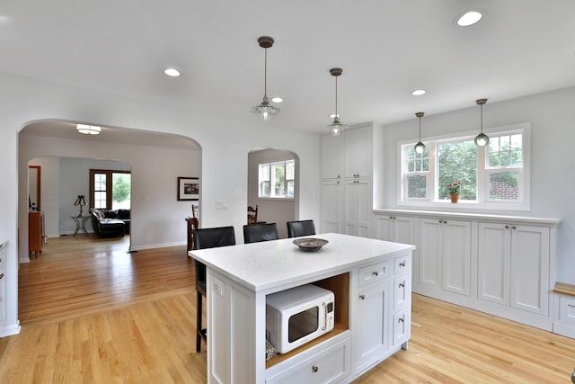 2009 Zollinger Rd, Columbus, OH 43221 - kitchen featuring arched walkways, white microwave, a kitchen breakfast bar, light wood finished floors, and white cabinets
