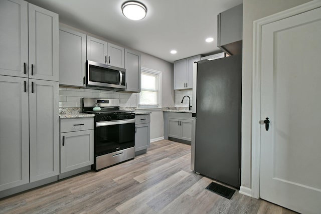 2567 Joyce Ave, Columbus, OH 43211 - kitchen with appliances with stainless steel finishes, gray cabinets, backsplash, light wood-style flooring, and light stone countertops