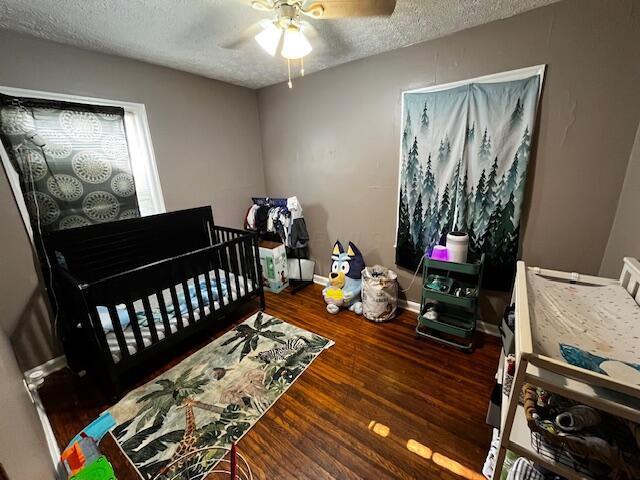 1231 E 23rd Ave, Columbus, OH 43211 - bedroom featuring a textured ceiling, wood finished floors, baseboards, a crib, and a ceiling fan