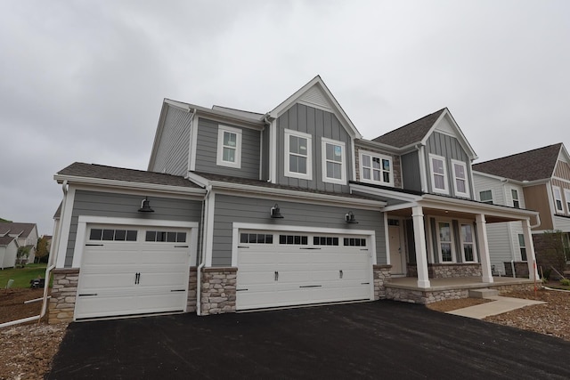 6946 Stillhouse Ln, Dublin, OH 43016 - view of front of home featuring covered porch, board and batten siding, asphalt driveway, an attached garage, and stone siding